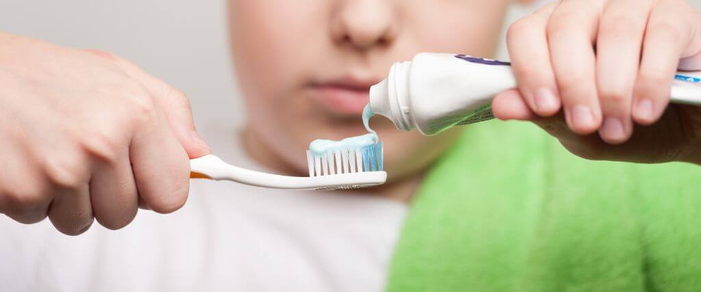 Boy putting toothpaste on his toothbrush.